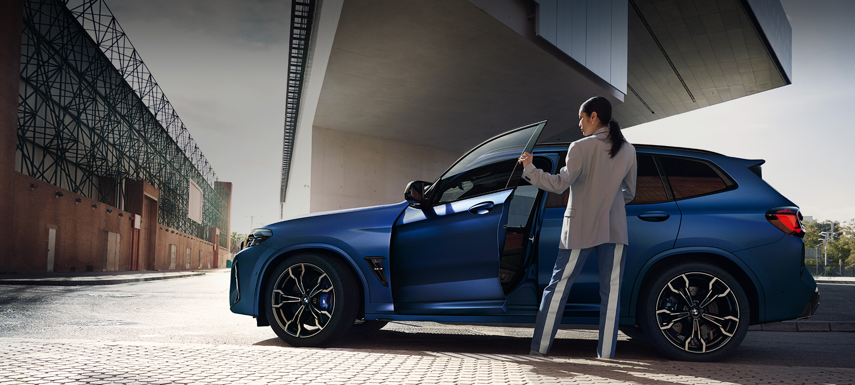 BMW X3 M Competition F97 LCI restylage 2021 BMW Individual Frozen Portimao Blau metallic Vue de profil en stationnement avec portière ouverte et mannequin femme